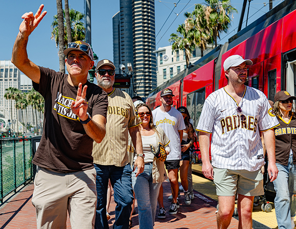 People wearing Padres jerseys and shirts in a crowd next to the Trolley