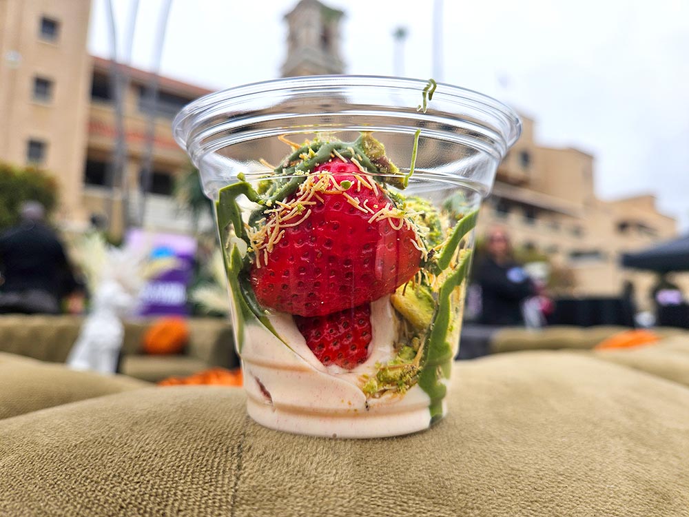 A plastic cup filled with strawberries, white chocolate, and pistachio cream.