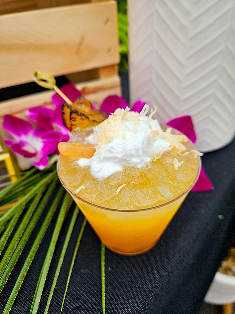 A plastic cup with juice in it, topped with cream with orchid flowers and a leaf.