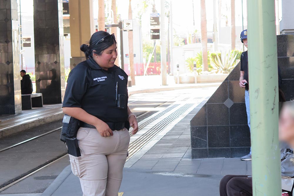 A woman in uniform stands talking to someone off screen at a transit center.