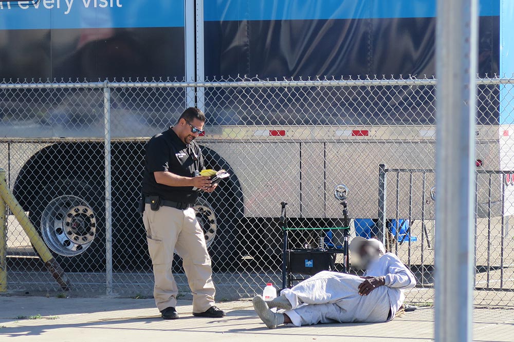 A man in uniform stands talking to an unsheltered individual in front of a bus.