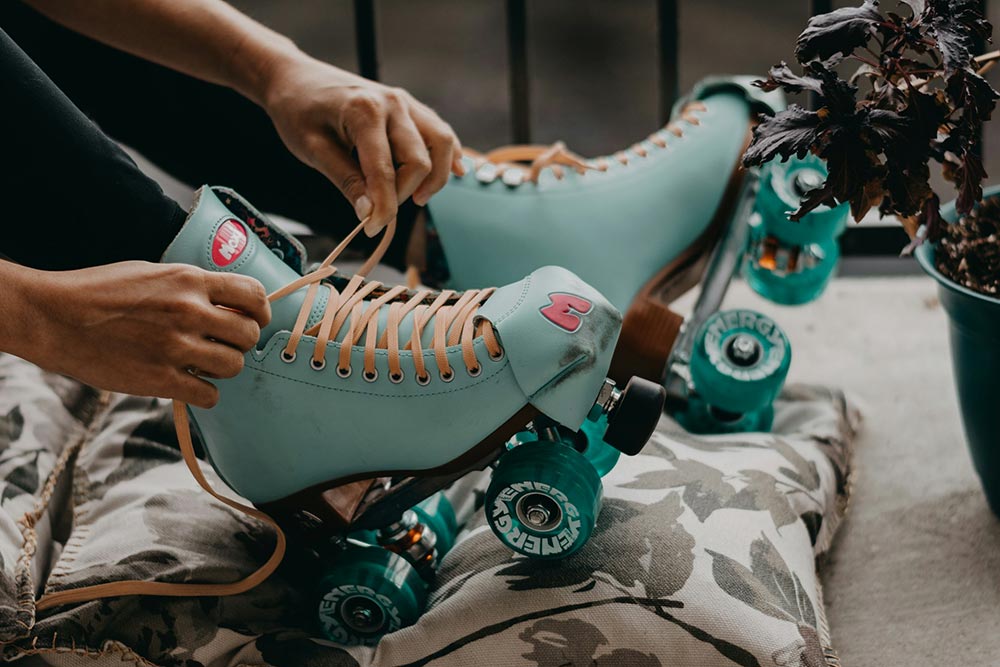A person tying the shoelaces on a pair of retro blue roller skates