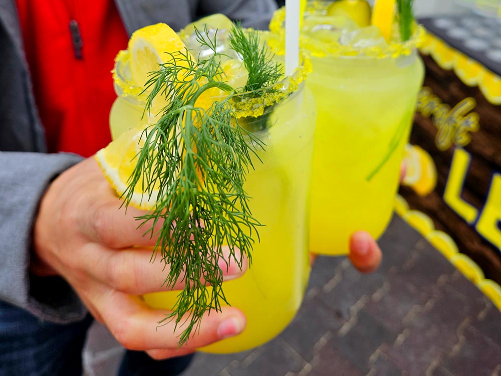 Hands holding two glasses full of pickle lemonade.