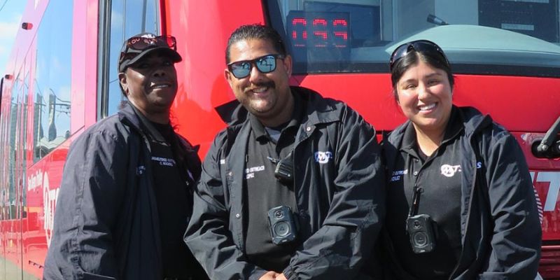 The MTS Homeless Outreach Team stands smiling in front of a San Diego Trolley.