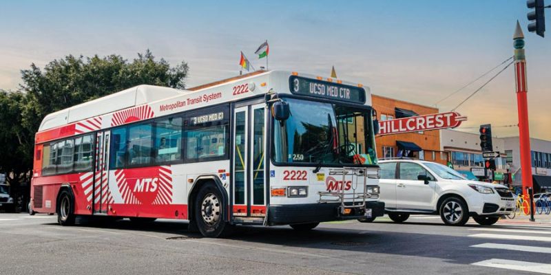Bus on the road with a white vehicle next to it and the Hillcrest sign in the background