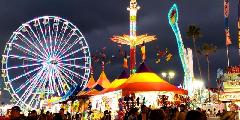 San Diego County Fair - Rides lit up at night with a large crowd and game tents.