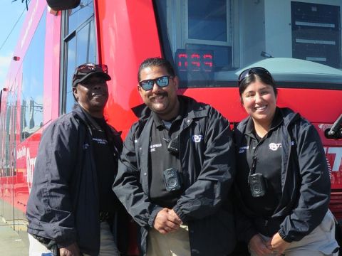 The MTS Homeless Outreach Team stands smiling in front of a San Diego Trolley.