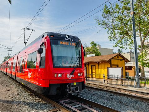 Trolley on the Orange Line in La Mesa on the tracks with a building and trees next to it