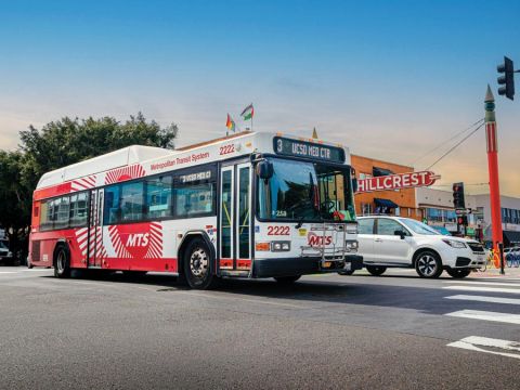 Bus on the road with a white vehicle next to it and the Hillcrest sign in the background