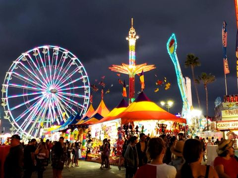 Dark cloudy sky at dusk with lit up rides and a crowd of people at the San Diego County Fair.