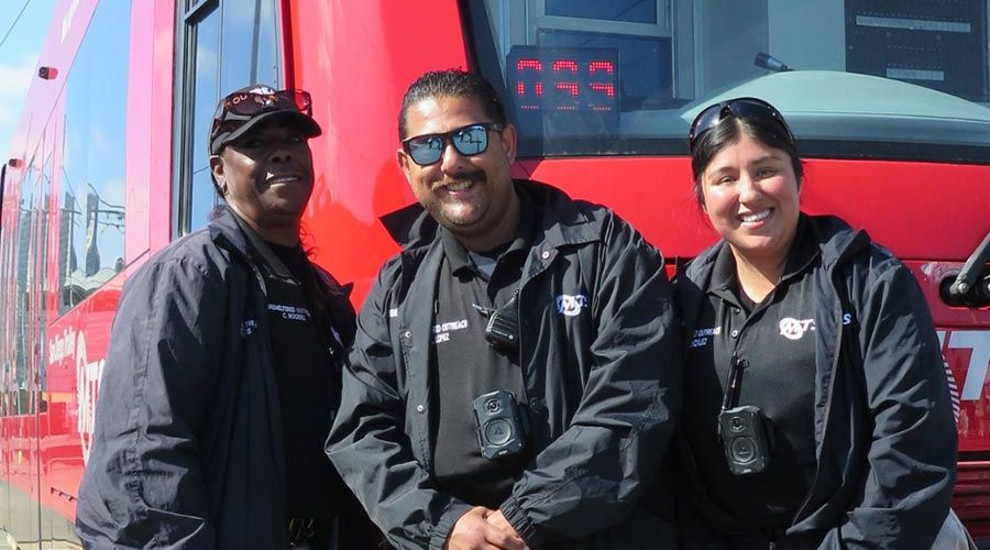 The MTS Homeless Outreach Team stands smiling in front of a San Diego Trolley.