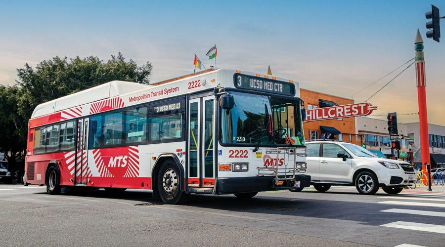 Bus on the road with a white vehicle next to it and the Hillcrest sign in the background