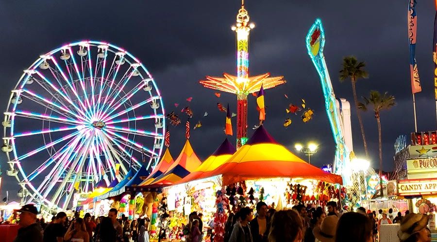 Dark cloudy sky at dusk with lit up rides and a crowd of people at the San Diego County Fair.