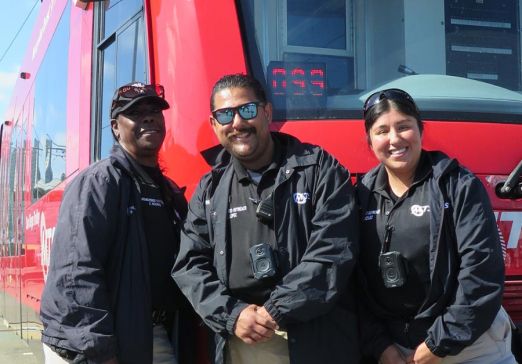 The MTS Homeless Outreach Team stands smiling in front of a San Diego Trolley.