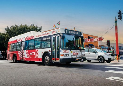 Bus on the road with a white vehicle next to it and the Hillcrest sign in the background