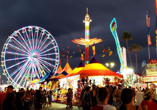Dark cloudy sky at dusk with lit up rides and a crowd of people at the San Diego County Fair.