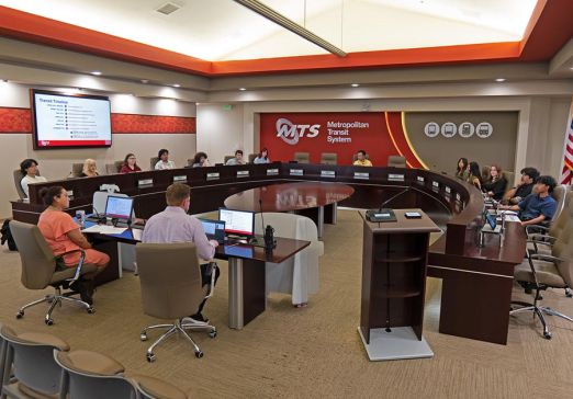 The Youth Advisory Council meets in the MTS Board room, with people sitting around a dais horseshoe platform.