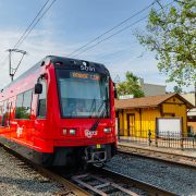 Trolley on the Orange Line in La Mesa on the tracks with a building and trees next to it
