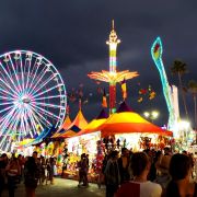 Dark cloudy sky at dusk with lit up rides and a crowd of people at the San Diego County Fair.